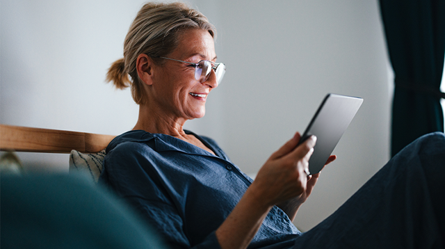 Close up shot of an older woman sitting and relaxing in her pajamas in the bed at home and reading from a tablet